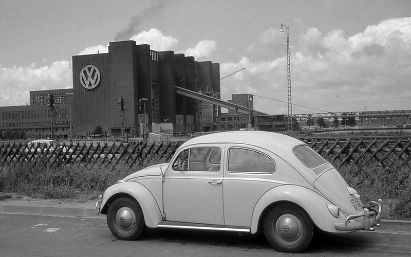 Finished VW Beetle parked in front factory.